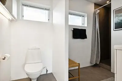 a white bathroom with a toilet and a window at Minimalist Coziness By The Wild North Sea in Harboør