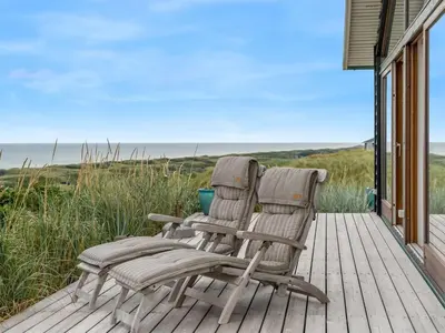 two chairs sitting on a deck with the ocean in the background at Holiday Home Bjerund - 300m from the sea by Interhome in Løkken