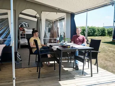two people sitting at a table outside of a camper at Toftum Bjerge Camping & Cottages in Humlum