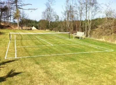 a tennis court with a net on a grass field at Romance And Sea View At Havbakken in Fjerritslev