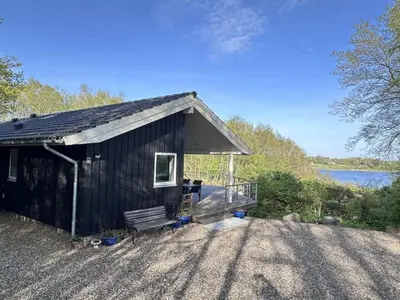 a small black building with a bench and a lake at Holiday Home Nico - 70m to the inlet by Interhome in Roslev