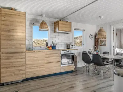 a kitchen with wooden cabinets and a table with chairs at Holiday Home Alrike - 200m from the sea by Interhome in Brovst