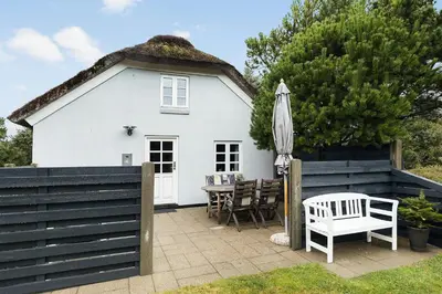 a white cottage with a thatched roof and a table and an umbrella at Natural Gem Between Heath And Dunes in Thisted