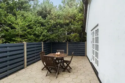 a table and chairs on a patio with a fence at Natural Gem Between Heath And Dunes in Thisted