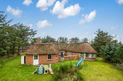 a house with a thatched roof and a playground at Family-Friendly Holiday Home With Pool And Spa Close To The North Sea in Harboør