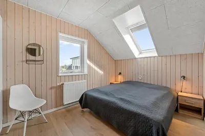 a bedroom with a bed and a white chair at Pool House With Activity Room, Built In 2020, With A View Of The North Sea in Nørre Vorupør