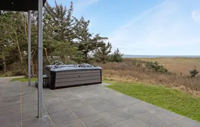 a hot tub sitting on a patio next to a field at Beach Front Home In Thyholm With Sauna in Thyholm