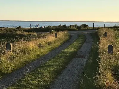 a dirt road next to a field with the ocean at Kornloftet i Lodbjerg in Vestervig