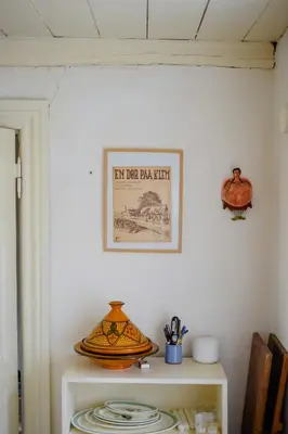 a picture on a wall above a table with plates at Cut Branches, Make Fire And Gaze At Treetops in Nykøbing Mors