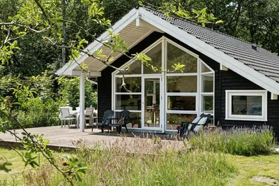 a small black cottage with a deck with a table and chairs at Forest House With Stream By Hjarbæk Fjord in Højslev