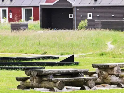a group of logs in a field with a house at 4 star holiday home in Brovst in Brovst