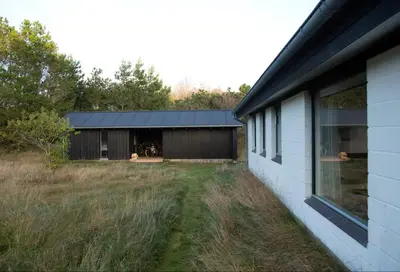a house with a yard next to a building at Dune House Near Bulbjerg in Frøstrup