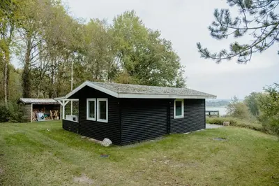 a small black house in a field with trees at Cozy Holiday Home With Forest And Fjord Views in Roslev