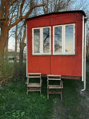 a red tiny house with two chairs and a window at Cozy Wagon House With Views Over The Limfjord in Roslev