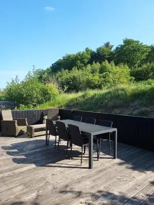 a table and chairs on a wooden deck with a hill at Holiday home golf house in beautiful Himmerland Farsø in Farsø