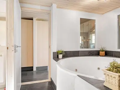 a white bathroom with a tub and a mirror at Holiday Home Elni - 350m from the sea by Interhome in Blokhus