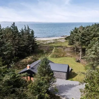a black building on a hill next to the ocean at Holiday Home In 1St Row By The Limfjord in Thyholm