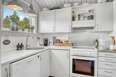 a white kitchen with white cabinets and a sink at Beautifully Renovated Holiday Home With Covered Terrace And Wood-Burning Stove, Close To The North Sea In Thy in Sønder Vorupør