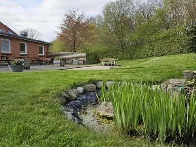 a stream in a yard with a bench and a table at Cozy Danish Room for Solo Stays in Lemvig