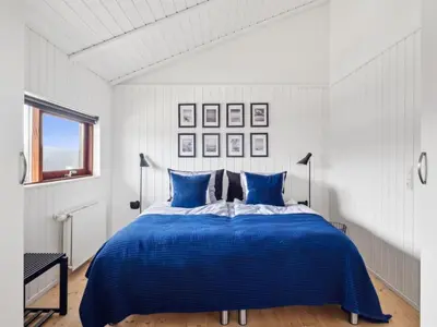 a white bedroom with a blue bed with blue pillows at Holiday Home Sinika - 100m from the sea by Interhome in Blokhus