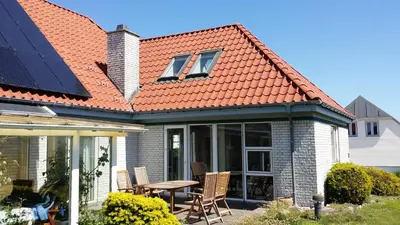 a house with an orange roof with a table and chairs at Bed & Breakfast i Vorupør in Nørre Vorupør