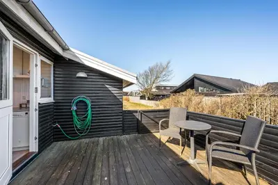 a deck with a table and chairs and a green hose at Pirupshvarrevej 5A in Blokhus