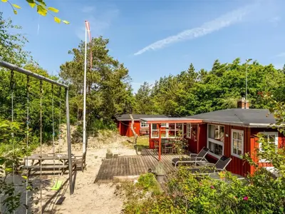 a red house with a picnic table and benches at Holiday Home Goodje - 400m from the sea by Interhome in Blokhus