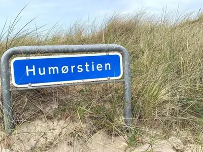 a blue street sign sitting in the sand at 4 star holiday home in Thyborøn in Thyborøn