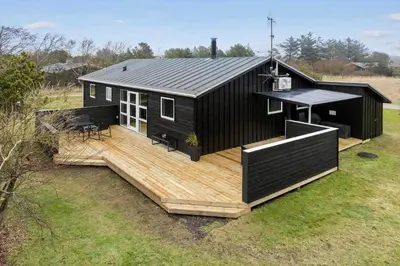 a black house with a wooden deck in a field at 1322-Snedsted-Lykkens-Hab-21 in Snedsted