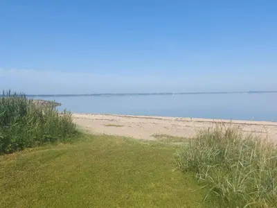 a sandy beach with grass and the ocean in the background at Holiday home for family in Denmark in Løgsted