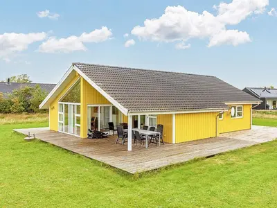 a yellow house with a wooden deck in a field at 10 person holiday home in Brovst-By Traum in Brovst