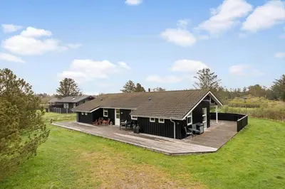 a black house with a deck in a field at LK1325-Lokken-Karinavej-59 in Løkken