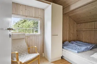 a bed in a room with a window and a chair at LK626-Lokken-Magdalenevej-40 in Løkken