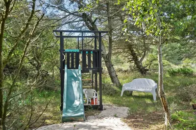 a playground with a slide and a chair in the woods at BL1440-Blokhus-Moreavej-2 in Blokhus