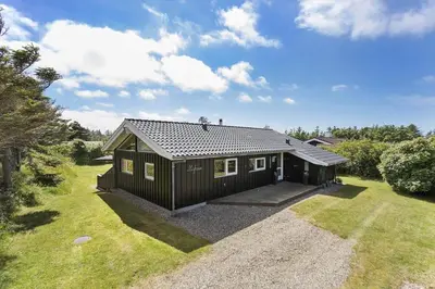 a black cabin with a porch in a yard at BL1201-Blokhus-Stromsvej-1 in Blokhus