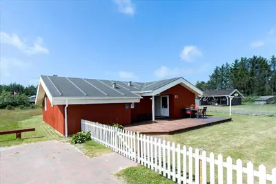a red house with a white fence in a yard at LK504-Lokken-Kristavej-23 in Løkken