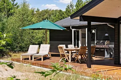 a wooden deck with a table and chairs and an umbrella at BL1535-Blokhus-Saetergaardsstien-5-A in Blokhus