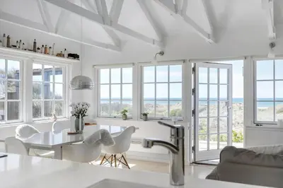 a white kitchen with a table and chairs and windows at LK1990-Lokken-Lottesvej-27 in Løkken