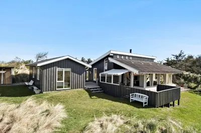 a black house on a grassy field with a bench at BL124-Blokhus-Klitvejen-75-a in Blokhus