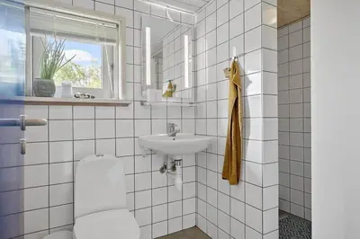 a white tiled bathroom with a sink and a toilet at BL1235-Blokhus-Malinsvej-9 in Blokhus