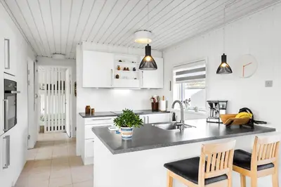 a kitchen with white cabinets and a sink and chairs at BL1349-Pandrup-Rodhus-Klitvej-217 in Pandrup