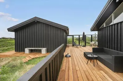 a black house with a wooden deck with a bench at BL1450-Blokhus-Klitvejen-99 in Blokhus