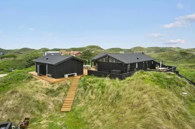 a couple of black buildings on a grassy hill at BL1450-Blokhus-Klitvejen-99 in Blokhus