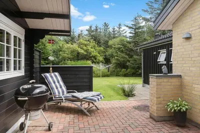 a grill and a chair on a brick patio at BL1396-Blokhus-Laerkevej-8 in Blokhus