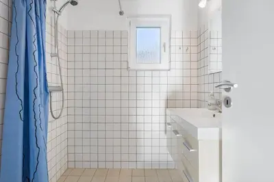 a white tiled bathroom with a shower and a sink at BL1359-Blokhus-Bellevueparken-24 in Blokhus