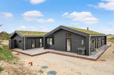 a black house with a deck in the sand at BL1740-Blokhus-Axel-P-Jensenvej-19 in Blokhus