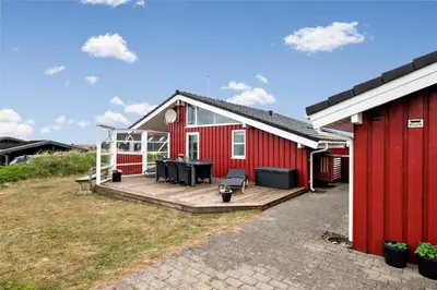 a red house with a wooden deck next to a building at BL330-Blokhus-Lyngvej-2 in Blokhus