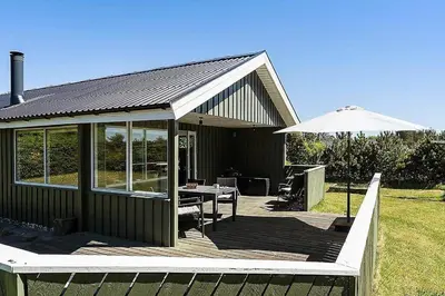 a house with a deck with an umbrella and a table at BL1366-Blokhus-Berberisvej-56 in Blokhus