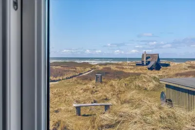 a view of the beach from a window with a bench at BL1449-Blokhus-Kienersvej-8 in Blokhus