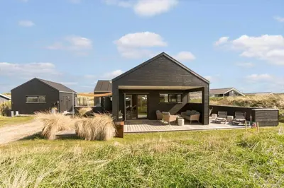 a black house with a deck in a field at BL1427-Blokhus-Ovesensvej-9 in Blokhus